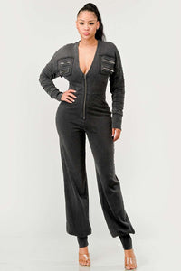 Multi Pocket Stretchy Black Jumpsuit | Rêve Dorés Model wearing a sleek black jumpsuit featuring a deep V-neckline, front zipper closure, and zippered pocket details on the chest. The fitted silhouette and cuffed ankles create a modern, edgy look perfect for casual or nighttime wear.