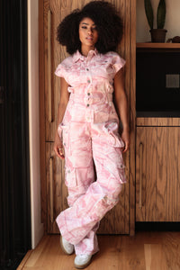Model wearing a pink utility-style jumpsuit featuring a button-up front, short sleeves, and cargo pockets for a functional yet stylish look. The relaxed fit and soft tie-dye pattern make it perfect for casual outings or chic everyday wear by Rêve Dorés