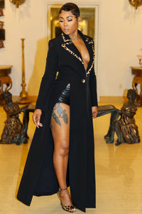 Femme Fatale
A poised woman stands in an ornately decorated interior, exuding elegance and sophistication. She is dressed in a sleek, form-fitting black gown or coat adorned with dramatic, oversized floral appliqués in a rich, animal-print fabric along the neckline. Her hair is styled in a polished, sleek look, and she accessorizes with a delicate bracelet and strappy black heels. FEMME DE LUXE MUURSWAGG X ATHINA COLLECTION