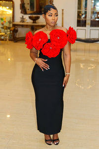 Fleur de Luxe
A confident woman stands in an elegant, vintage-inspired setting, wearing a refined black gown with eye-catching, oversized red floral embellishments along the neckline. The figure-hugging dress is paired with simple yet sophisticated black strappy heels. Her hair is sleek and stylishly arranged, and she accessorizes with a delicate bracelet and a gold watch. FEMME DE LUXE MUURSWAGG X ATHINA COLLECTION