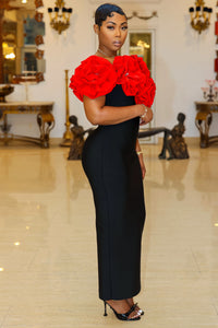 Fleur de Luxe
A confident woman stands in an elegant, vintage-inspired setting, wearing a refined black gown with eye-catching, oversized red floral embellishments along the neckline. The figure-hugging dress is paired with simple yet sophisticated black strappy heels. Her hair is sleek and stylishly arranged, and she accessorizes with a delicate bracelet and a gold watch. FEMME DE LUXE MUURSWAGG X ATHINA COLLECTION